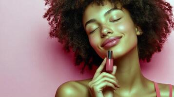 Young african female with curly hair enjoying lip gloss against pink background photo