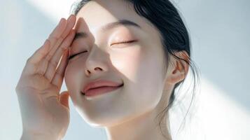 Young asian female smiling in sunlight with hand on forehead photo