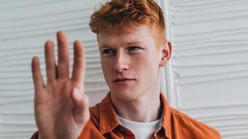 A young man with red hair making a stop sign photo