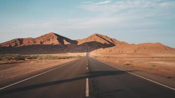 An empty road in the desert with mountains in the background photo