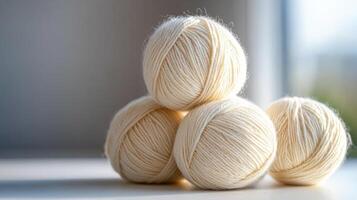 Cream colored wool yarn balls stacked on light surface, soft texture photo