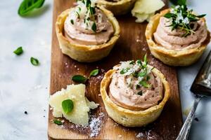 Savory tartlets filled with rich smoked mackerel mousse garnished with herbs and parmesan cheese photo