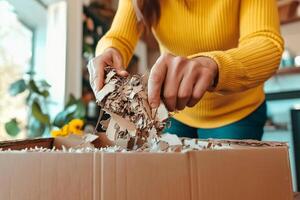 A woman is opening a cardboard box with shredded paper photo