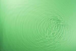 Concentric waves of green water droplets spreading over the surface of the water illuminated with green light photo