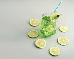 Mint cocktail garnished with lemon slice and green cherry surrounded by lemon slices on white table photo