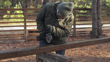 A person is grinding a metal rail in a wooded area, sparks flying as they focus on the task. The surrounding landscape is filled with trees and a relaxed atmosphere. video