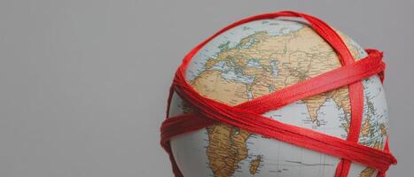 A globe wrapped in red rubber bands, symbolizing restrictions or limitations on travel and connectivity. photo