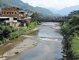 Emerging market economic trends Concept. A scenic view of a river flowing through a small town, flanked by greenery and buildings, with mountains in the background under a partly cloudy sky. photo