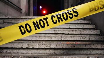 Yellow Do Not Cross tape stretched across a stairway at a potential crime scene with blurred police lights in the background video