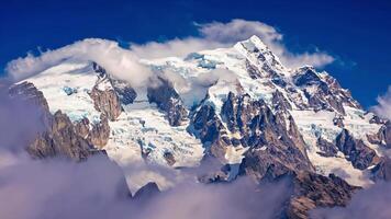 Snow covered mountain peak rising above the clouds with a deep blue sky in the background video