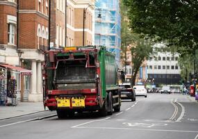 A green garbage truck navigates a London street, symbolizing the city dedication to sustainability amid a backdrop of classic British architecture.. photo