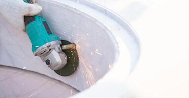 With a skilled hand and a steady grinding machine, a worker transforms a rough construction weld nut into a sleek white curve marble storage piece. photo