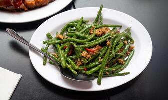 Stir fried string beans with minced pork in a savory garlic sauce, garnished with red chili slices for a flavorful kick. photo