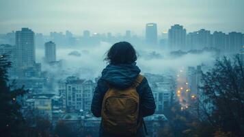 A woman with a backpack standing on a hill overlooking a city photo