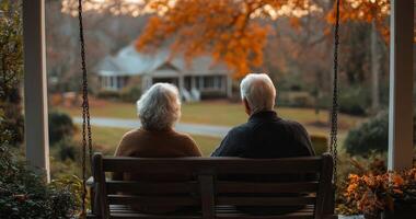 An elderly couple sitting on a swing in front of a house photo