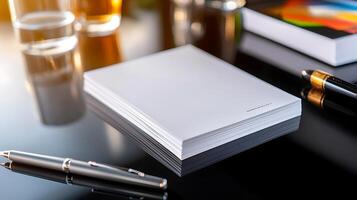 A clean, blank notepad on a reflective surface with a pen and drinks in the background photo