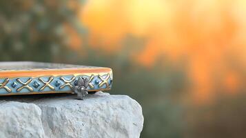 A beautifully crafted decorative frame resting on a stone, with a blurred natural background photo
