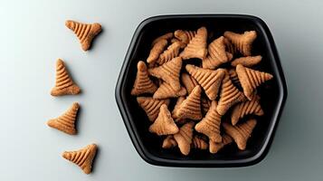 A close-up view of a black bowl filled with triangular-shaped snacks on a light background photo