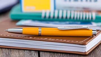 A close-up of a vibrant yellow pen resting on a brown notebook, surrounded by office supplies photo