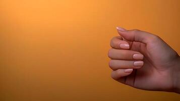 A graceful hand with neatly manicured nails against a warm orange background photo