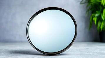 Round mirror on a textured surface with a blurred green plant in the background photo