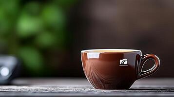 A close-up of a brown coffee cup on a wooden table with greenery in the background photo