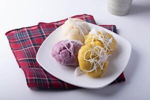 plate of colorful steamed rice cakes topped with shredded coconut sits on red plaid cloth, creating vibrant and appetizing display photo