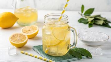 refreshing lemonade in mason jar with ice and lemon slices, accompanied by fresh lemons and straw, evokes sense of summer photo