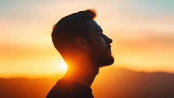 silhouette of man with glowing sunrise in background creates serene and contemplative atmosphere. warm colors of sky enhance peaceful mood photo