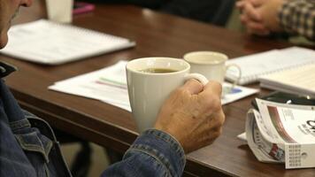 person holding coffee mug during meeting at table with documents and notebooks. setting suggests casual yet focused atmosphere, with participants engaged in discussion photo