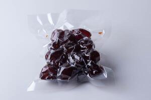 vacuum sealed package of dark red dates on white background. packaging is clear, showcasing glossy texture of dates inside photo