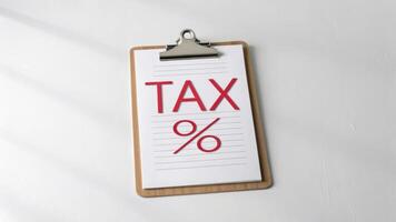 clipboard with TAX written on it in bold red letters and percentage symbol below, placed on white surface photo