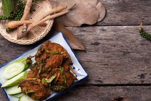 plate of spicy fried crab garnished with fresh herbs and served with cucumber slices on rustic wooden table, accompanied by basket of fresh ingredients photo