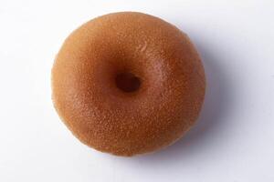 plain, glazed donut sits on white background, showcasing its smooth texture and classic round shape. donut golden brown color highlights its freshly baked appearance photo
