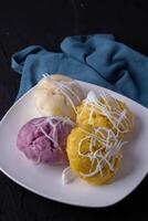 plate of colorful steamed rice cakes topped with shredded coconut, set against dark background with blue cloth. vibrant colors and textures create inviting and appetizing presentation photo