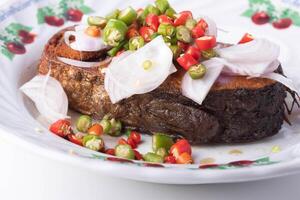 plate of fried fish topped with sliced onions and colorful chili peppers, showcasing vibrant and spicy dish. fish is crispy and golden brown, served on decorative plate with floral pattern photo