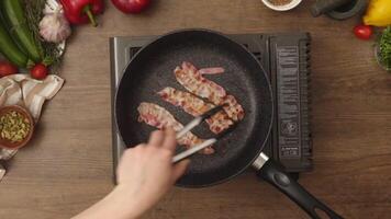 Overhead view of person turning bacon frying in pan video