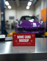 A red name card mockup stands on a metallic surface in a blurry auto repair shop with a purple car in the background psd