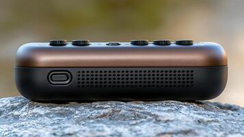 Close-up view of a sleek portable speaker resting on a textured stone surface in nature photo