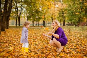 Plus-size woman in purple dress holding and playing with her 3-year-old daughter in warm autumn park. photo