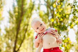 Young mother playing and tossing her one-year-old son in the park on sunny day photo