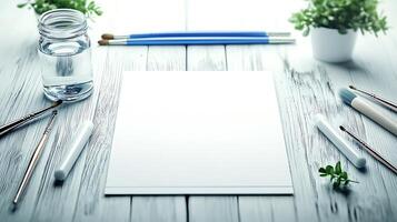 Blank canvas surrounded by art supplies on a wooden table with plants in the background photo