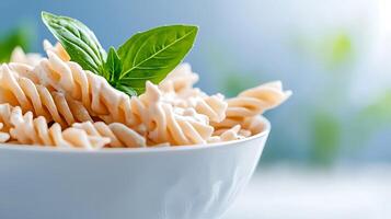 A close-up view of a bowl of creamy pasta with fresh basil leaves, set against a blurred background photo
