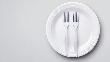 Two silver forks placed symmetrically on a white plate against a minimalistic gray background photo