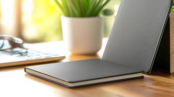 A minimalist workspace featuring an open notebook, a potted plant, and a laptop in soft natural light photo