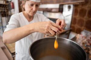 Baker woman adding eggs to a big industrial pan to prepare cupcakes. Cupcakes making photo