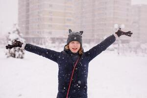 Portrait of happy 12 year-old girl in a warm jacket and a cat-ear hat under heavy snow photo