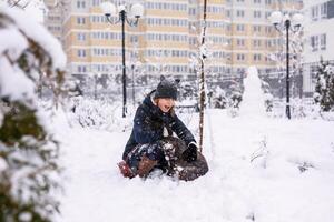 A girl sits with her dog in the snow in winter, throwing snowballs at her. Russian spaniel runs with flapping ears in the snow and plays photo