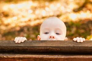 Almost bald baby boy peeking out from behind a wooden bench in warm autumn park photo