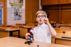 8-year-old smart schoolboy in glasses studying through a microscope photo